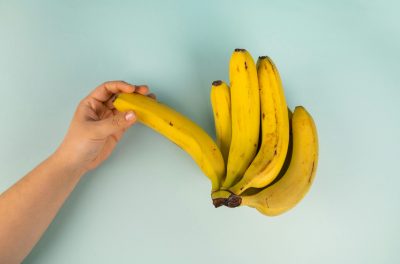 pexels-photo-7194921-7194921 A hand holding a bunch of ripe, fresh bananas against a light background, showcasing their vibrant yellow color.